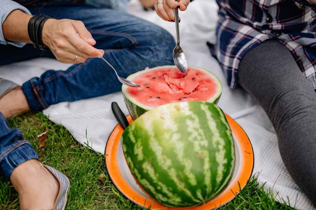 a couple scooping fresh watermelon with spoons